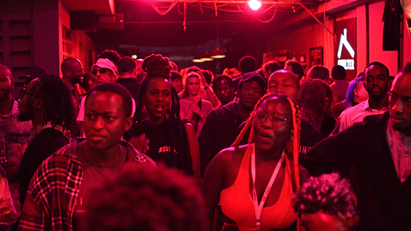 audience of a night event organised by the Santuri organisation in Nairobi. the group of people is positioned under a red neon light 